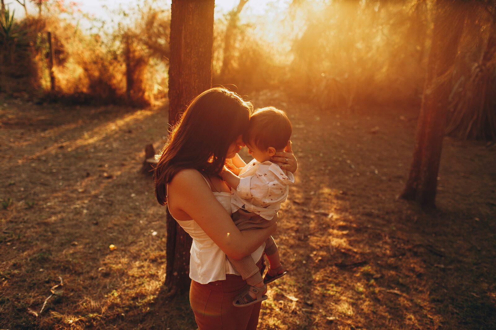 Madre sosteniendo a su bebé en un bosque cálido al atardecer